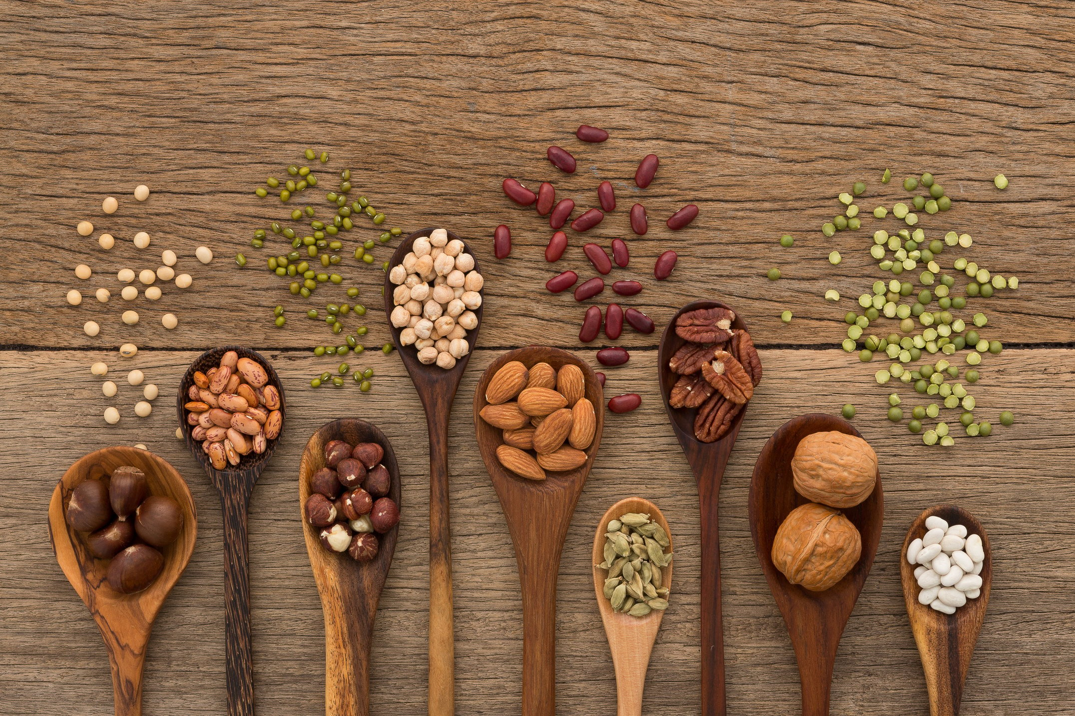 Different kind of beans and lentils in wooden spoon on wood background. mung bean, groundnut, walnuts, macadamia, almond, soybean, red kidney bean, black bean, sesame, corn, red bean and brown pinto beans